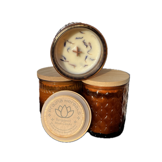 Three amber Prajna Ritual Candle jars with wood lids; one open reveals white wax, dried flowers, and a cross-shaped wick.